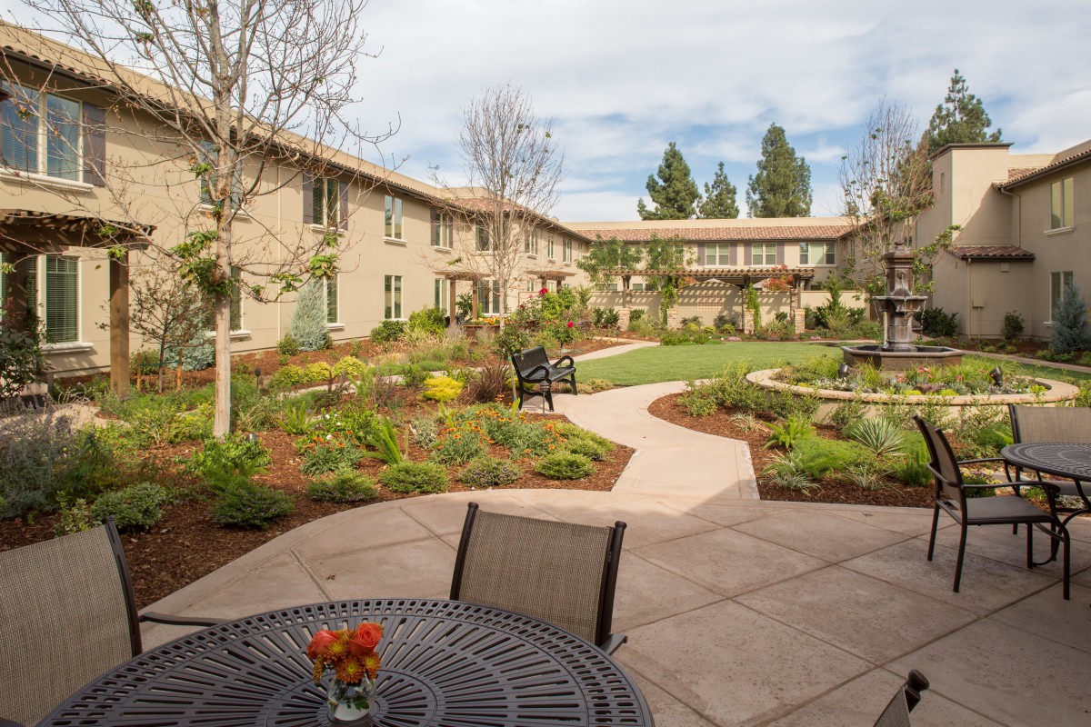 A tranquil courtyard with a garden path and seating area, surrounded by a two-story building.