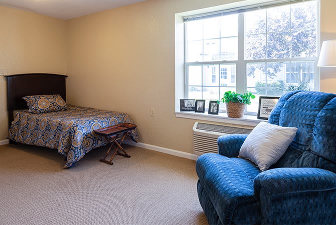 A cozy bedroom featuring a bed, a comfortable armchair, and a large window with decorative items on the sill.