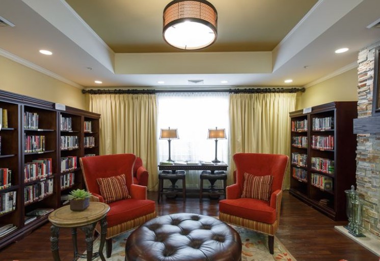 A cozy library living room with red chairs, bookshelves, and an ottoman.