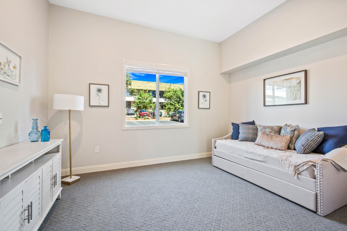 A bright and modern living room featuring minimalist decor with neutral colors, showcasing a comfortable sofa and a window with a view of greenery outside.