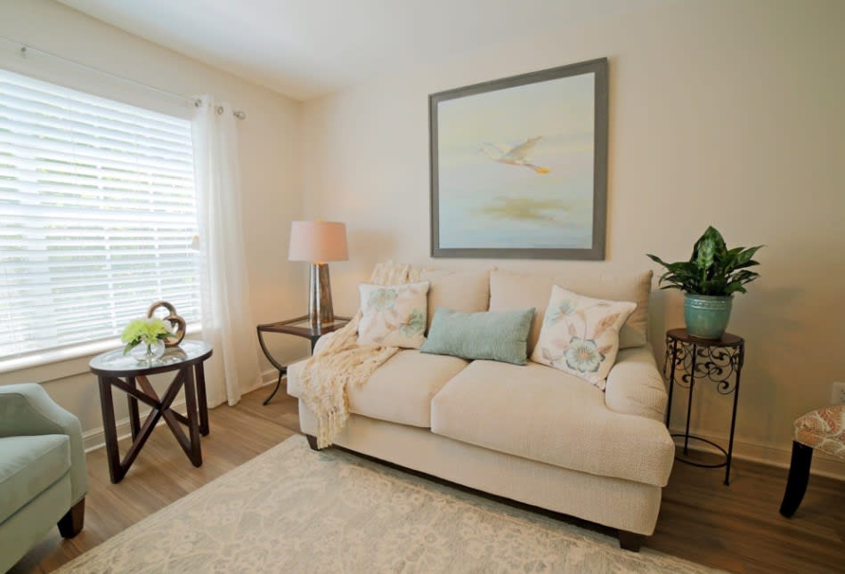 A cozy living room with a beige sofa adorned with pillows, a side table with a lamp, and a painting on the wall.