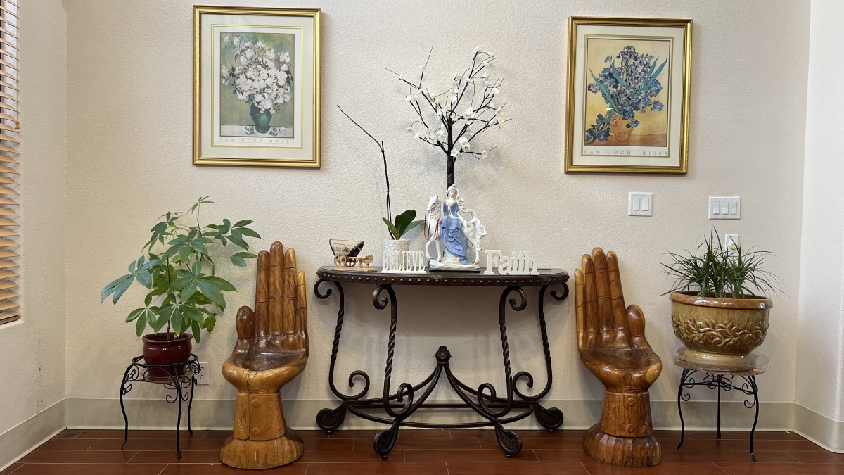 A stylish interior arrangement featuring a decorative table with a vase and plant, flanked by unique hand-shaped chairs and framed artwork on the wall.