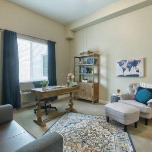 A well-lit home office with a desk, chair, bookshelf, and decorative elements.