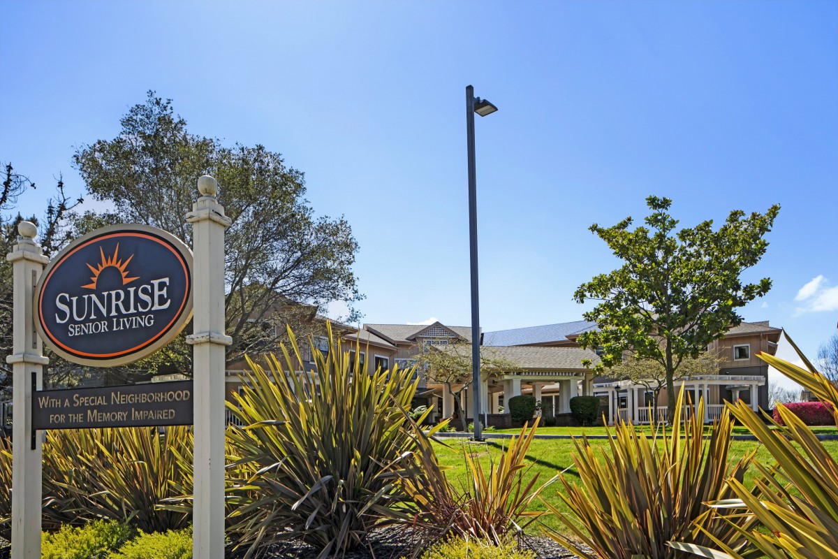 A scenic view of a building with a sign and lush greenery under a clear blue sky.