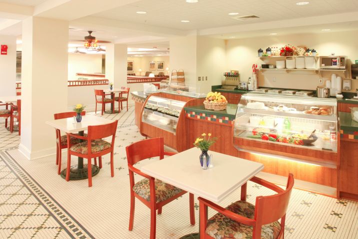 A cozy bakery and cafe interior with red chairs, tables, and display cases filled with pastries.