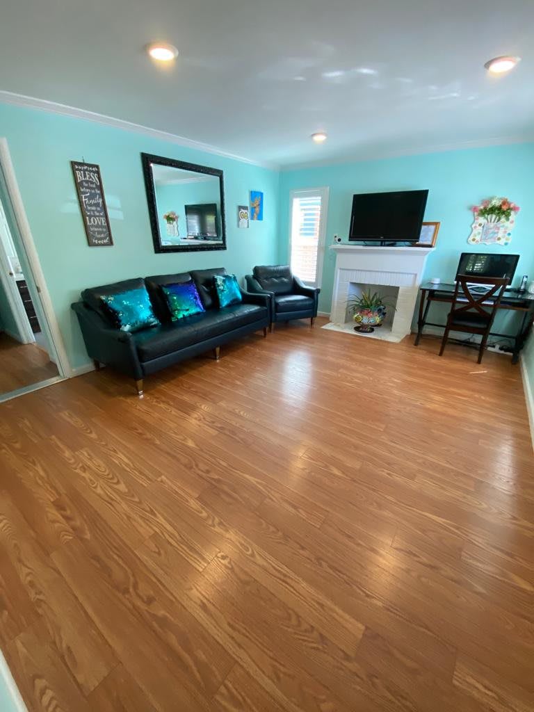 A spacious and brightly lit living room featuring a black sofa, television, and fireplace on a hardwood floor.