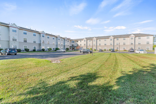 A view of a modern apartment building with a well-maintained lawn and parking area under a clear blue sky.