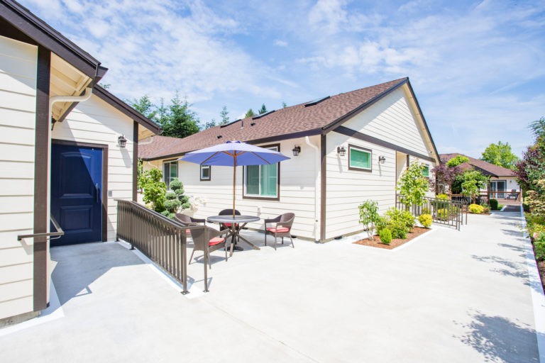 A modern house with a spacious patio area featuring outdoor seating and an umbrella on a sunny day.