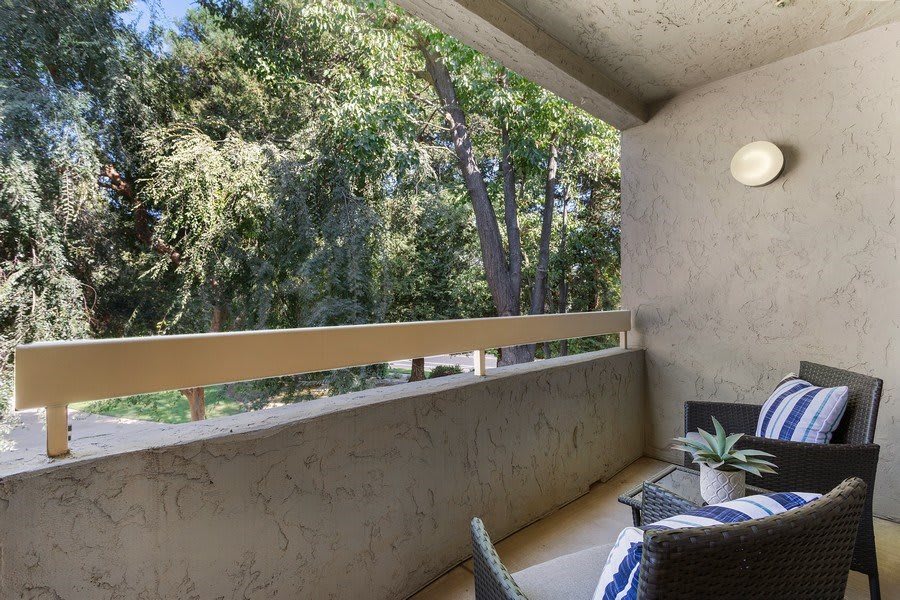 A cozy balcony overlooking a lush green area with outdoor furniture.
