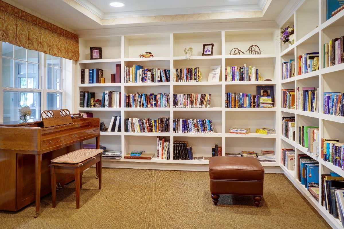 A cozy home library with a piano and bookshelves filled with books.