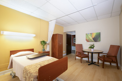 A spacious and well-lit room featuring a bed, a small dining area, and warm-colored walls.