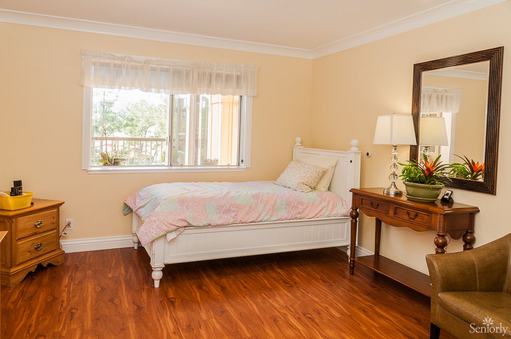 A cozy bedroom with a single bed, wooden floor, and a window letting in natural light.