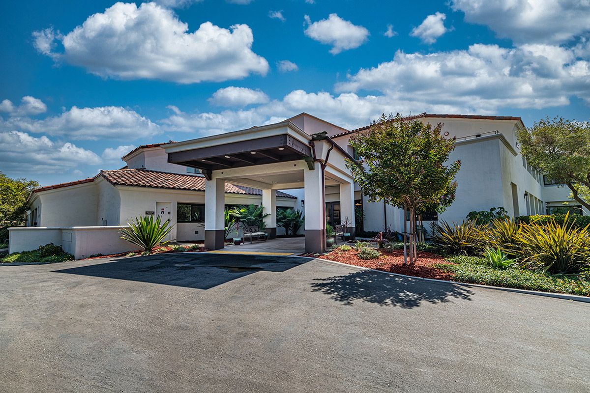 A building with a covered entrance and landscaped surroundings under a partly cloudy sky.