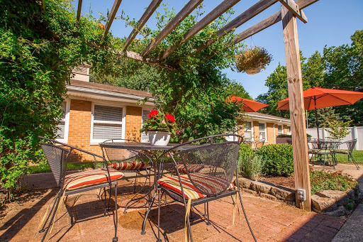 A cozy outdoor patio with a table and chairs, surrounded by greenery and vibrant flowers.