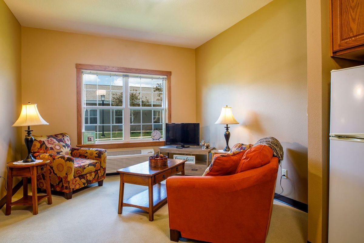 A cozy living room with a sofa, chairs, a TV, and a window providing natural light.