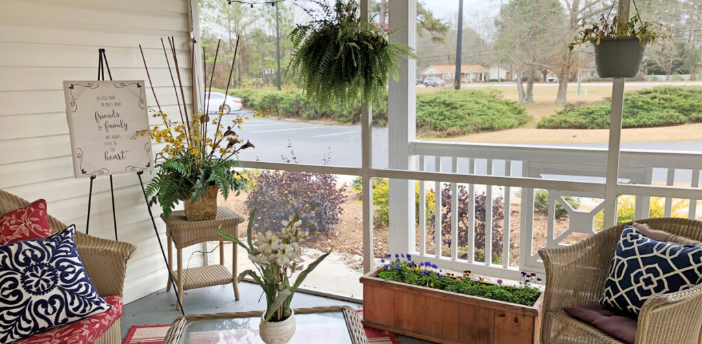 A cozy porch with a variety of plants and flowers, featuring a hanging plant, potted plant, and rectangular planter.
