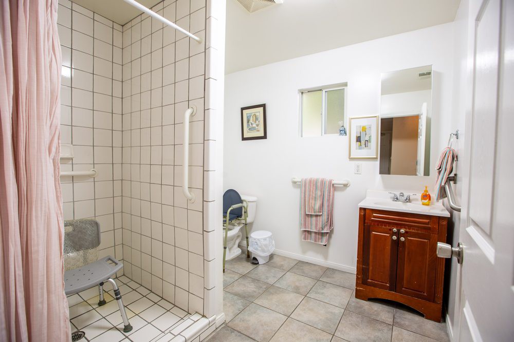 An accessible bathroom with a tiled shower area, equipped with a shower chair and a wooden vanity with a mirror.
