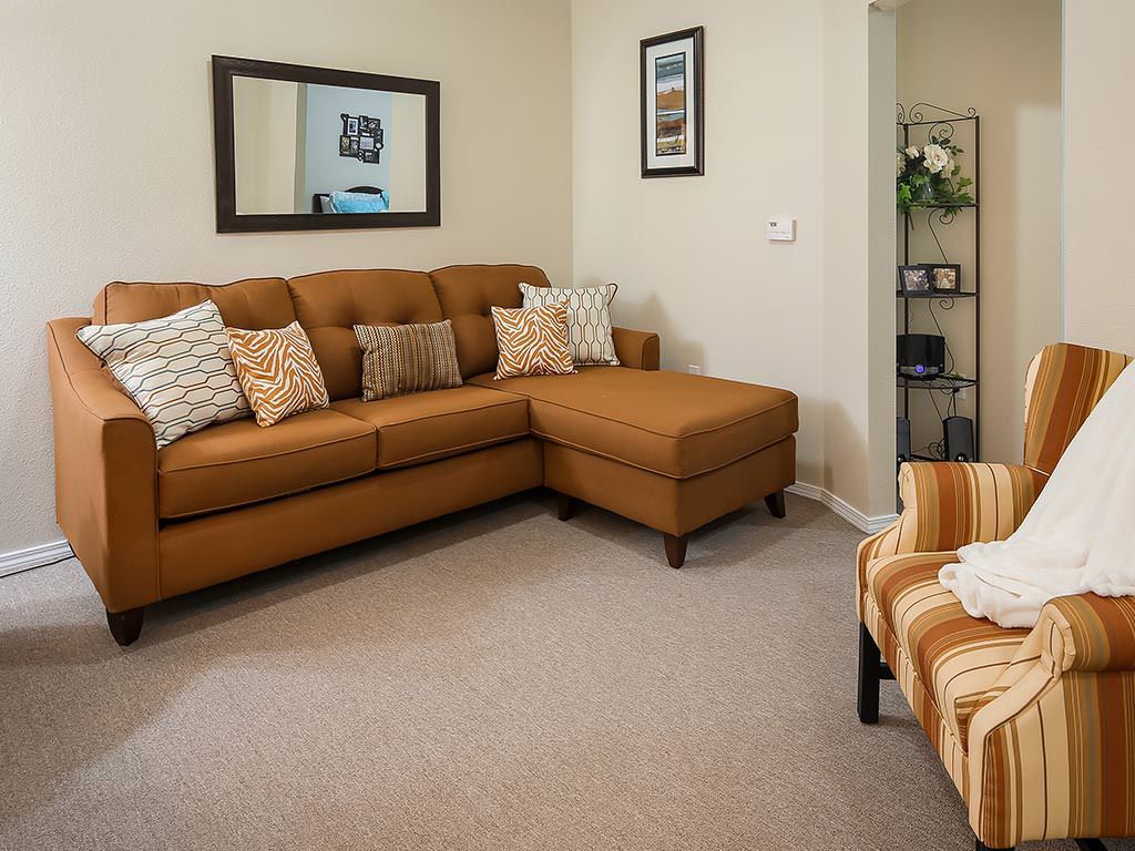 A cozy living room with a brown sectional sofa, decorative pillows, and an armchair, complemented by a large mirror and a bookshelf.