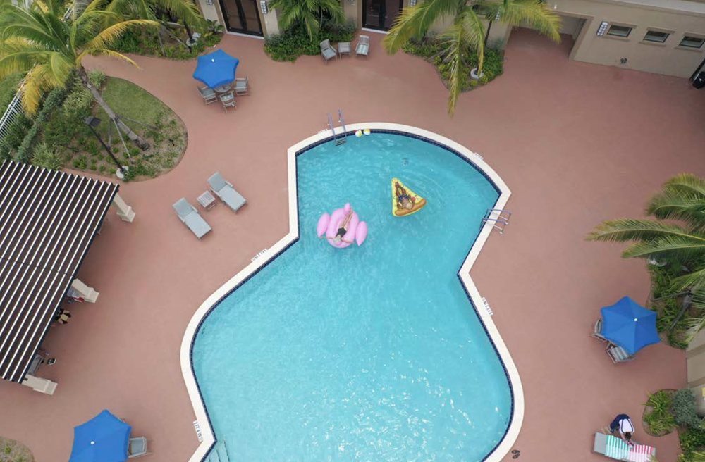 Aerial view of a uniquely shaped swimming pool with inflatable floats and surrounding patio furniture.
