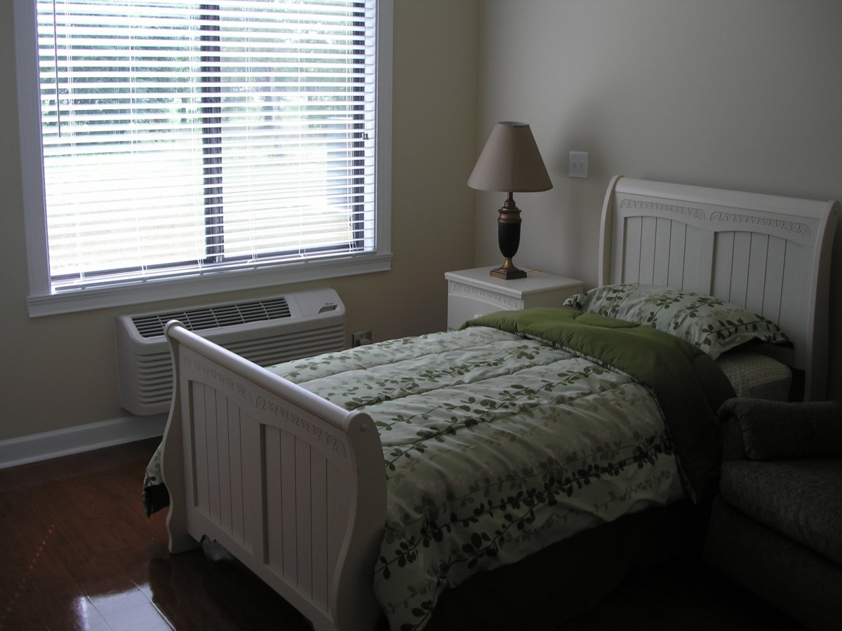 A cozy bedroom with a single bed, nightstand, and window with blinds.