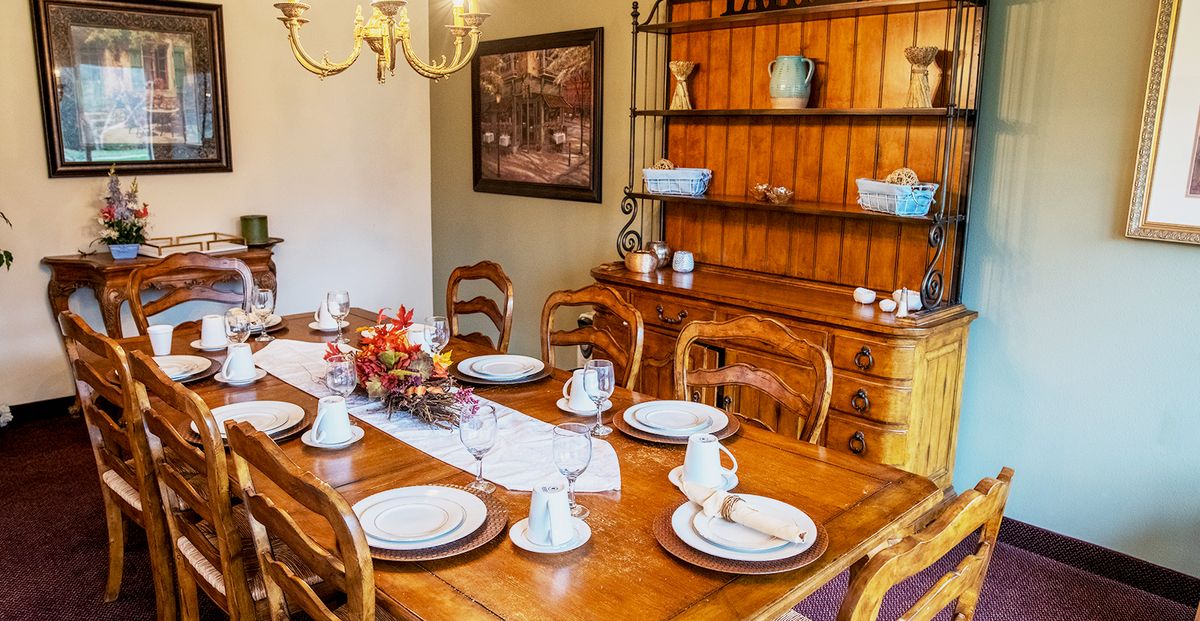 A cozy dining room with a wooden table set for dinner, featuring elegant dinnerware and surrounded by matching chairs.