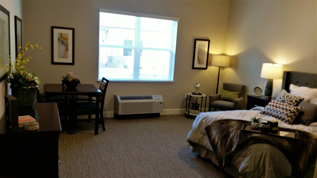 A cozy bedroom with a bed, chair, lamp, and window.