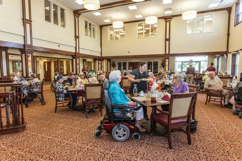 A group of elderly individuals enjoying a meal and socializing in a spacious dining area.