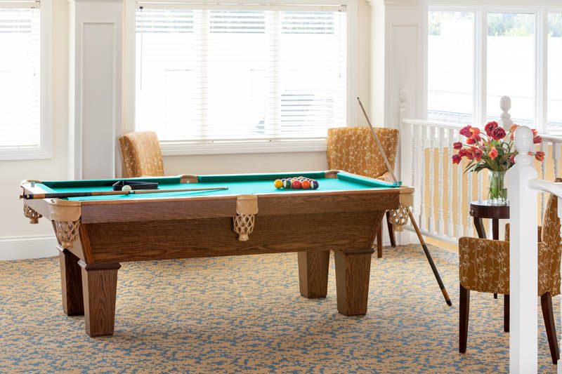 A cozy game room featuring a billiards table with cue sticks and chairs around it.