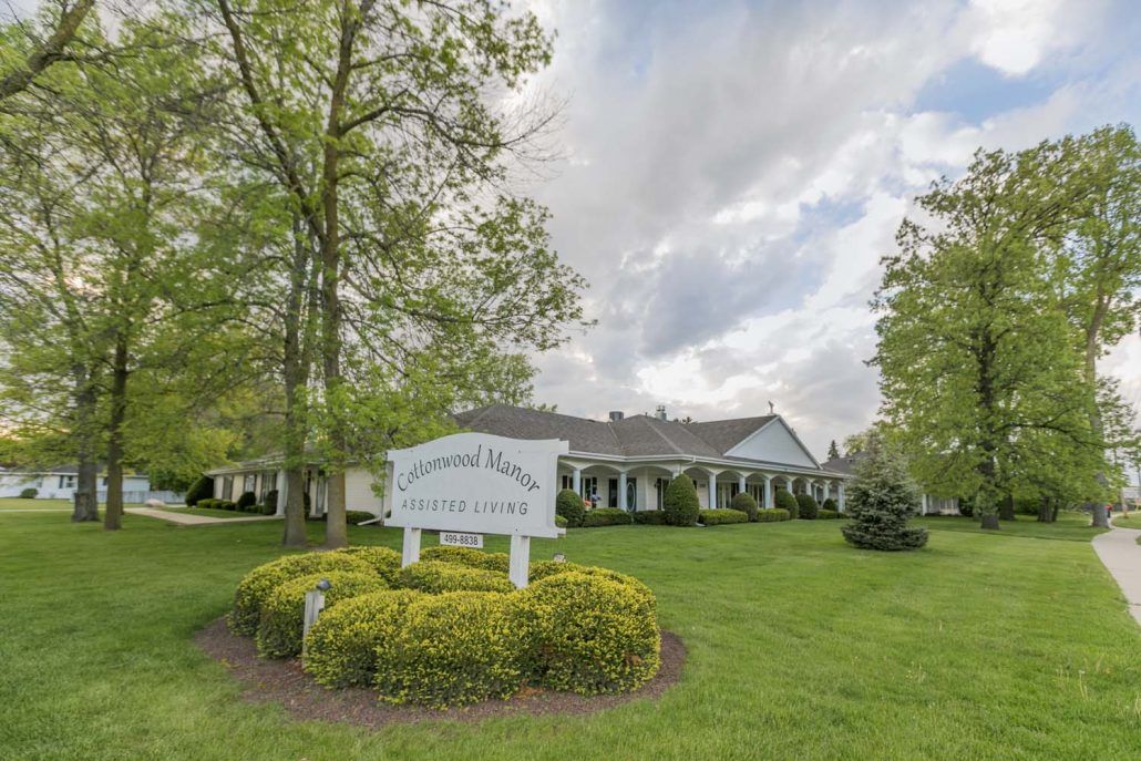 A house with a front yard and a sign surrounded by trees under a cloudy sky.
