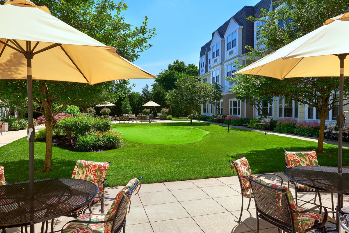 A sunny garden patio with furniture and umbrellas overlooking a well-manicured lawn.