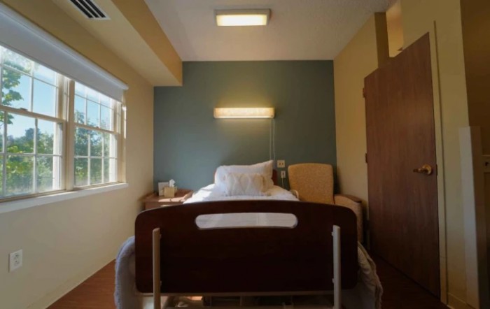 A well-lit hospital room featuring a single bed and a comfortable chair.