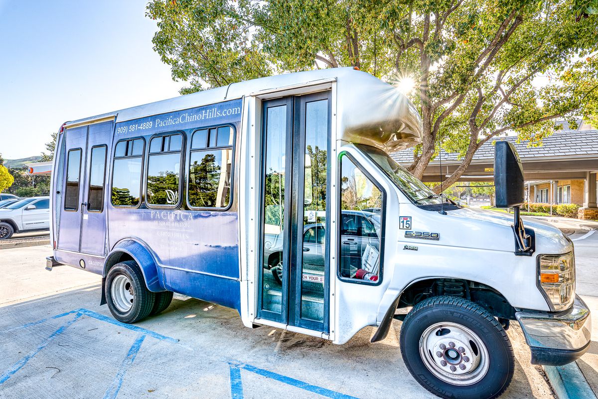 A blue shuttle bus parked in a lot surrounded by trees on a sunny day.