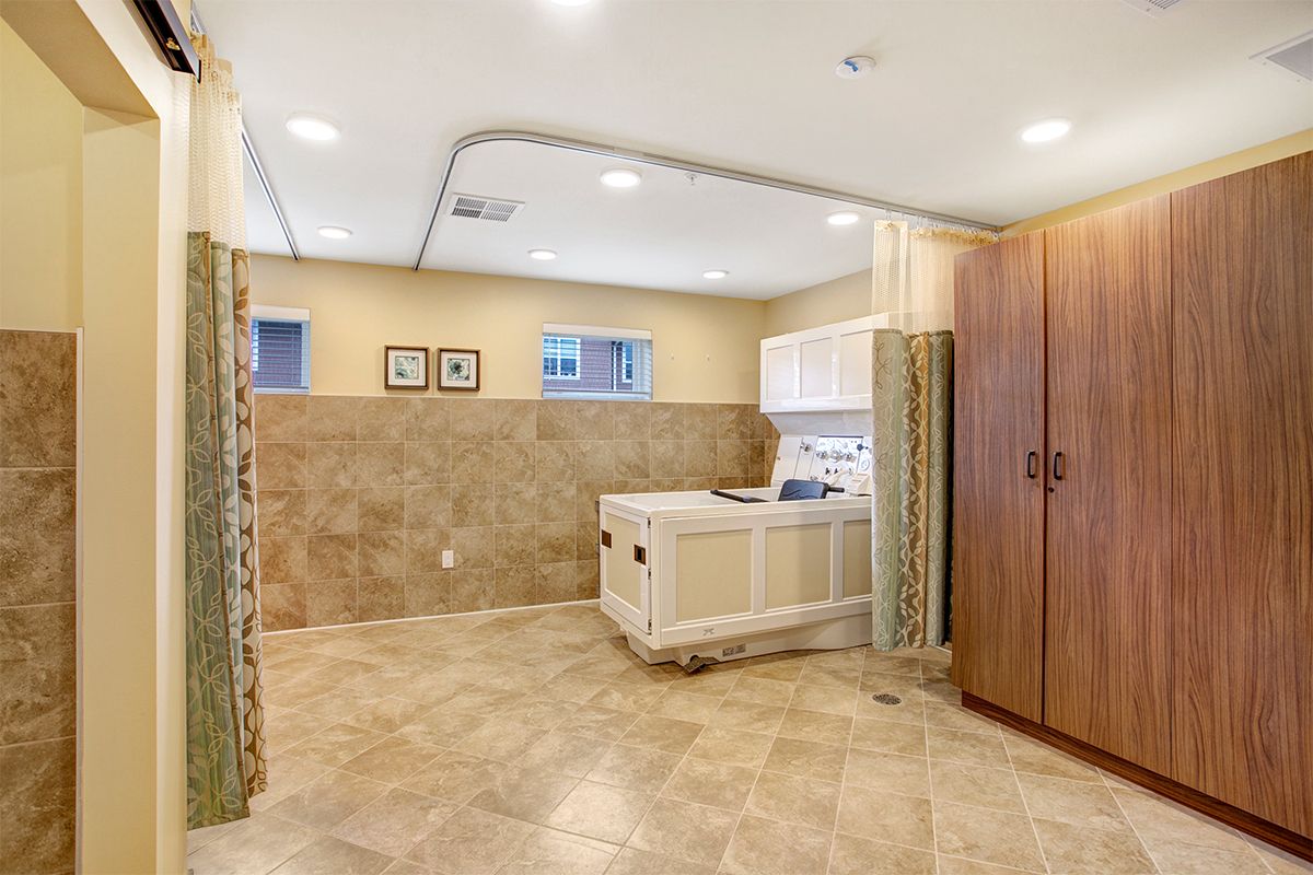 A spacious laundry room with tile flooring, featuring a utility sink, cabinets for storage, and a washing machine.