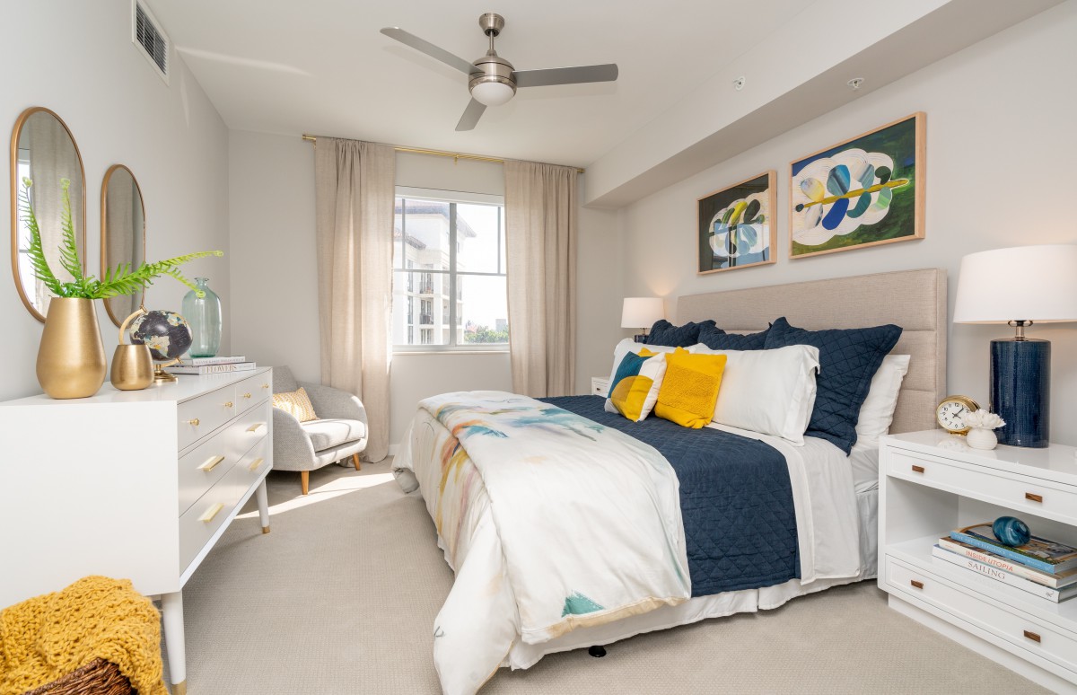A bright, modern bedroom featuring a stylish bed with navy and white bedding, decorative pillows, and abstract artwork on the walls.