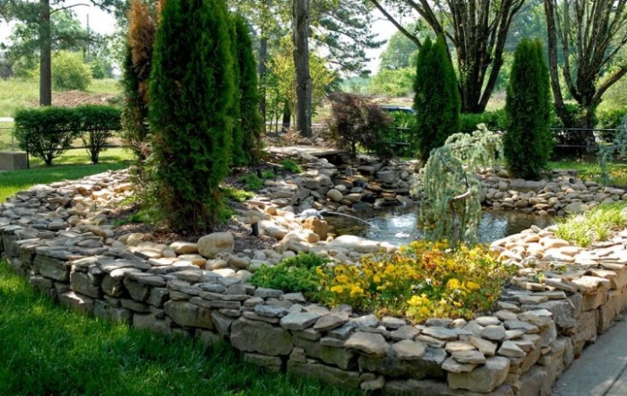 A beautifully landscaped garden featuring a pond surrounded by a stone wall and lush greenery.