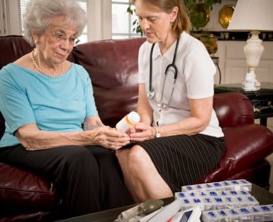 A nurse assists an elderly woman with her medication during a home visit.