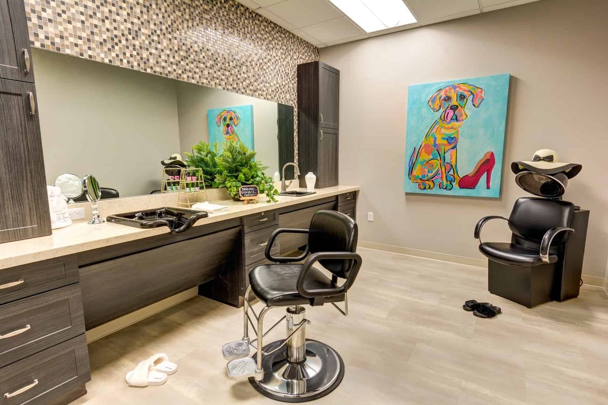 A modern barbershop interior featuring a stylish chair, large mirror, vibrant artwork, and decorative plants.
