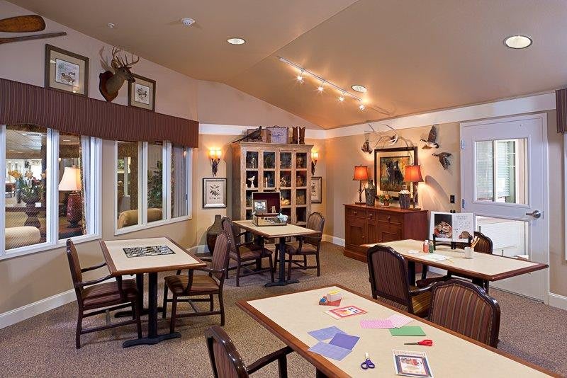 A cozy community room with tables and chairs, decorated with artwork and soft lighting.