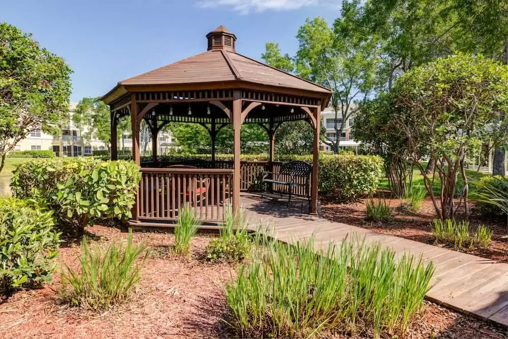 A wooden gazebo situated in a lush garden setting surrounded by greenery.