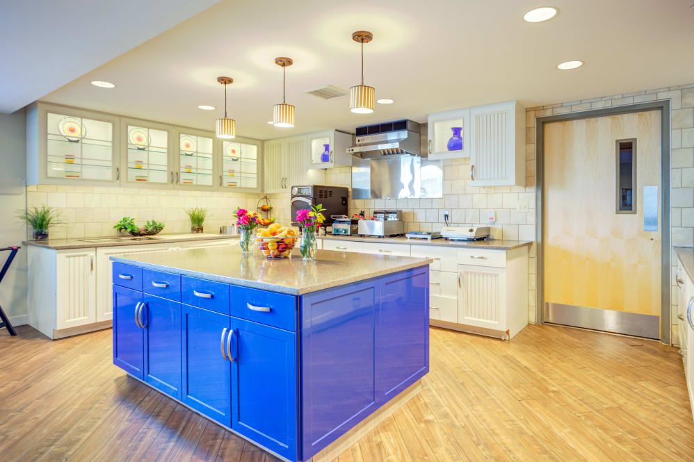 A modern kitchen featuring a vibrant blue island, wooden floors, and stylish pendant lighting.