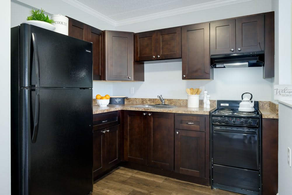 A modern kitchen with dark cabinets and black appliances, featuring wood flooring and a spacious countertop with a sink.