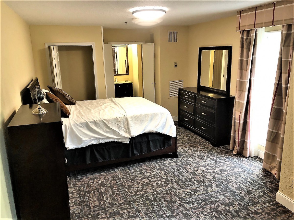 A well-furnished bedroom featuring a bed, dresser with mirror, and carpeted floor.