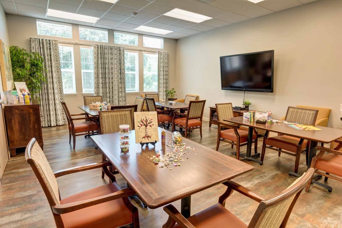 A well-lit dining room with multiple tables and chairs, featuring a large television on the wall.