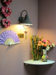 A cozy interior corner featuring a wall lamp, decorative fan, and a vase of colorful flowers.