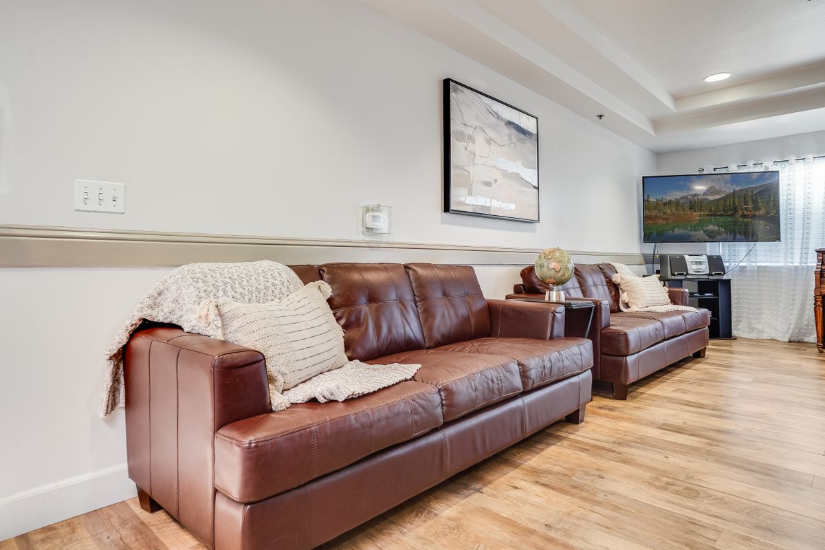 A cozy living room featuring leather sofas, decorative cushions, and a wall-mounted TV.
