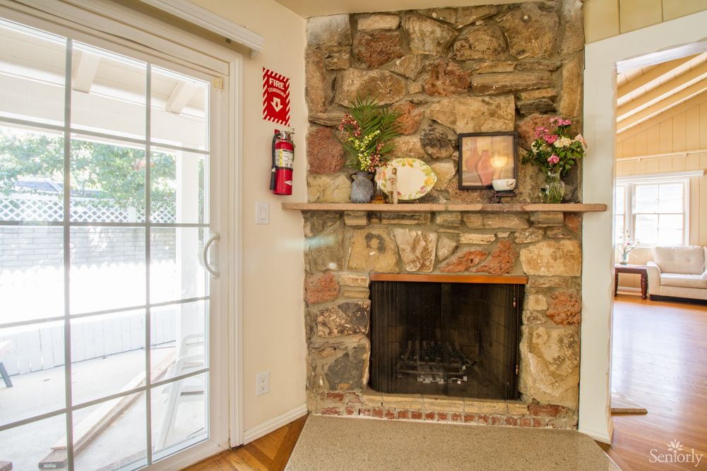 A cozy fireplace with a stone mantel, adorned with decorative items and a nearby sliding glass door.