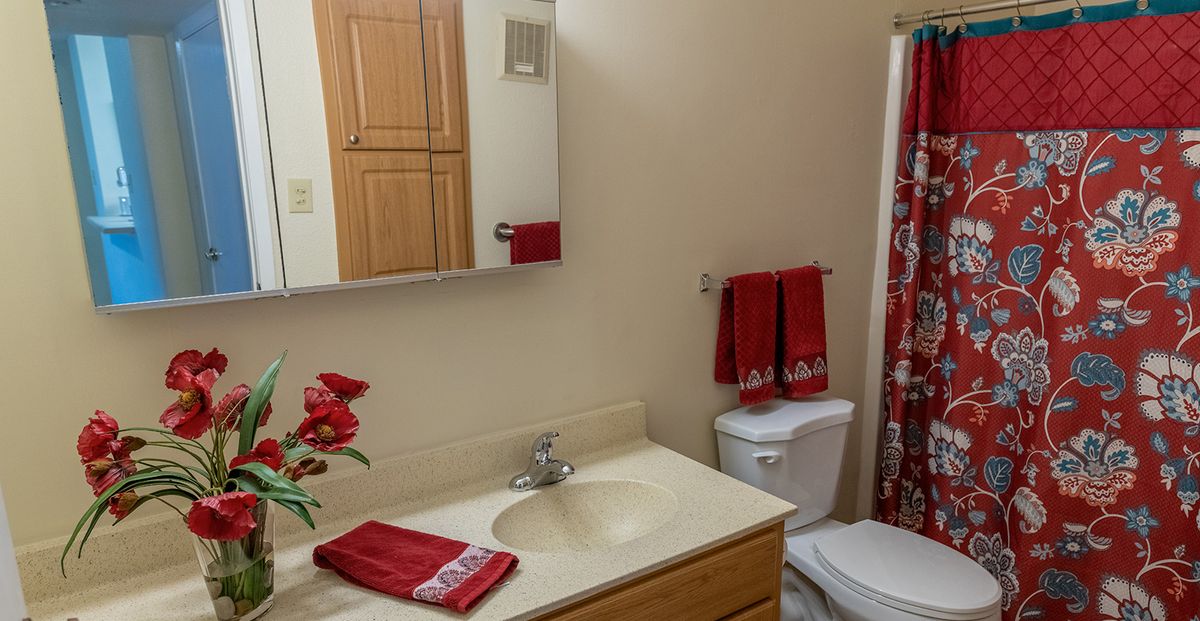 A neat bathroom with red accents and floral decor.