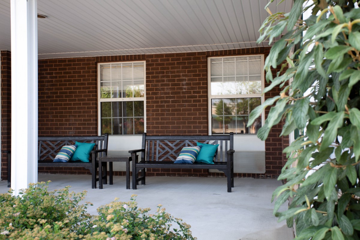 A cozy porch with benches adorned with colorful pillows, set against a brick wall.