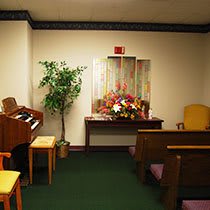 A small chapel room featuring an organ, pews, and a floral arrangement.