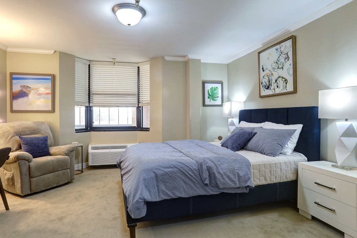 A cozy bedroom with a neatly made bed, two lamps, and framed artwork on the walls.